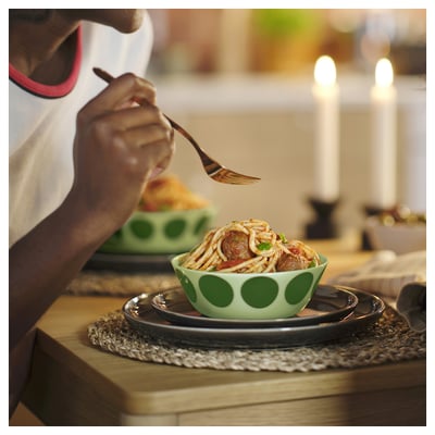 A person eating spaghetti from a green polka-dot bowl. Candles light the wooden table.