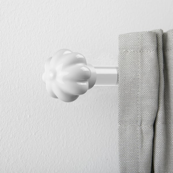 White ceramic curtain finial resembling a flower bud, securely attached to a grey curtain on a white wall.