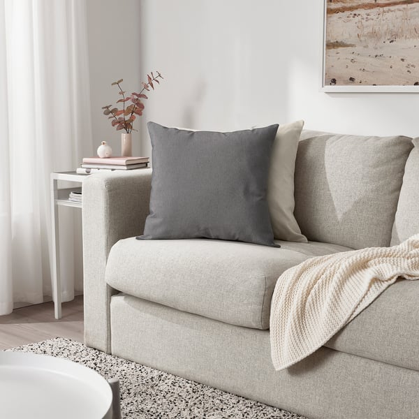 PARADISBUSKE cushion, grey, soft texture, square shape. Large size, sits on a sofa, near a vase.