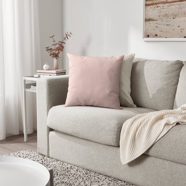 Cosy living room with grey sofa, pink/beige cushions, cream blanket, side table with vase and books.