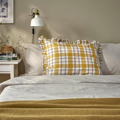Cosy bed with yellow checked PARKOLVON pillow, white lamp, small bedside table, framed art.