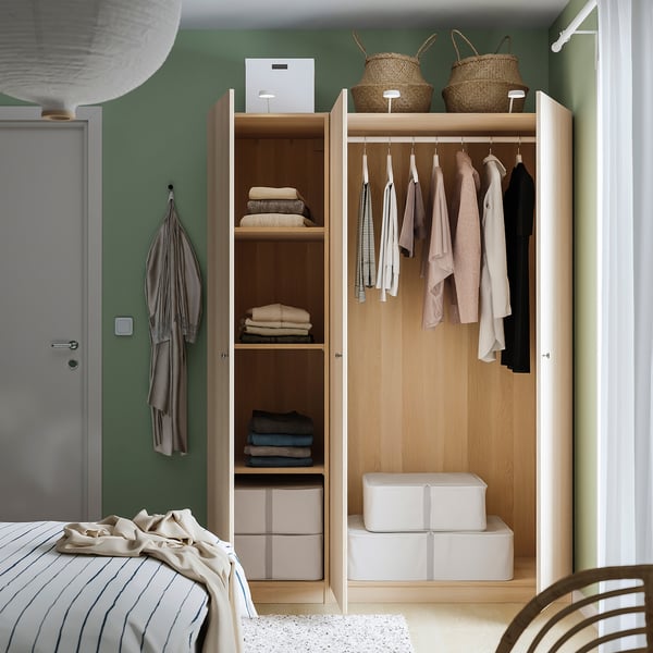 Wooden wardrobe with shelves and hangers, organising clothes and bedding near a bed.