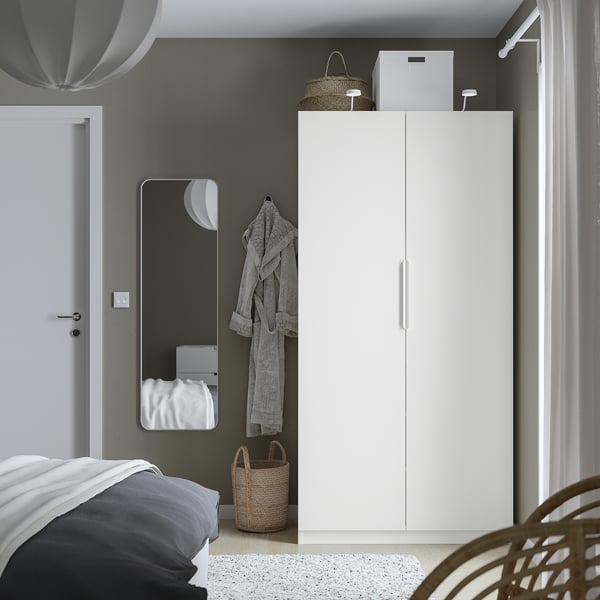 Minimalist bedroom featuring a white PAX wardrobe, tall and slim closet near a bed, grey wall, mirror, and hanging robe.