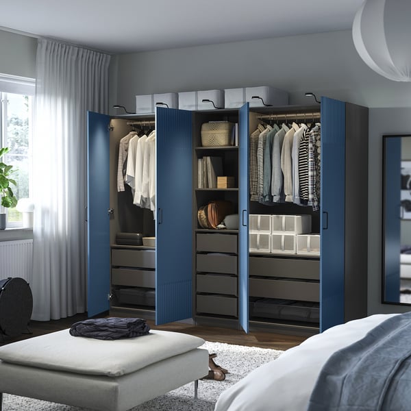 Blue PAX wardrobe in bedroom with clothes, white bed, patterned rug, tall window.