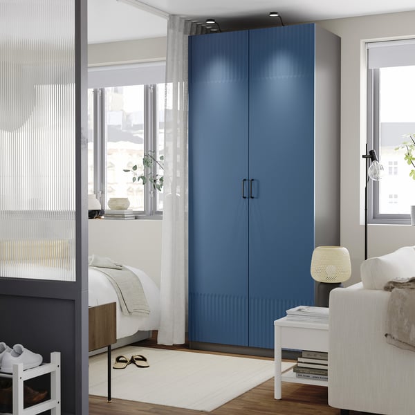 Modern bedroom with tall blue PAX wardrobe, white decor, and natural light.