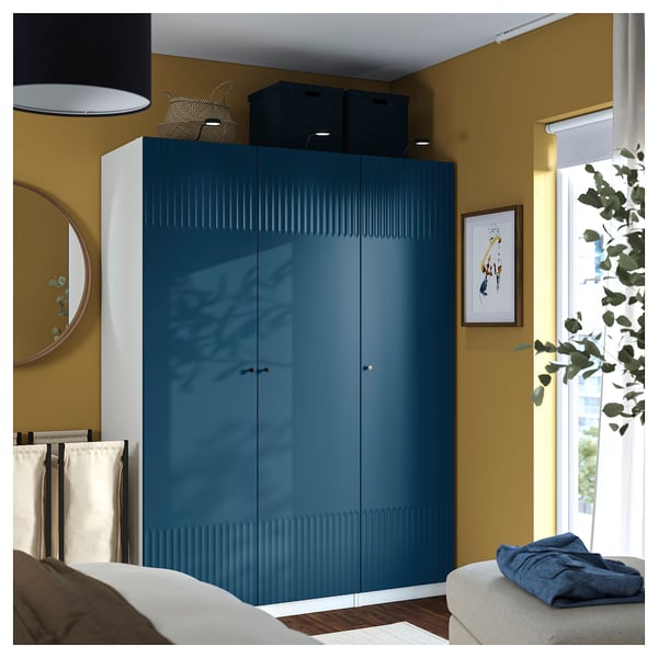 Modern bedroom with tall blue PAX wardrobe, large bed, white mirror, and window plant.
