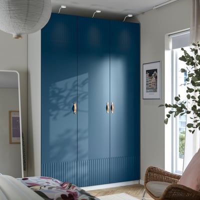 Modern bedroom with large blue PAX wardrobe, wicker chair, and floral pillow.