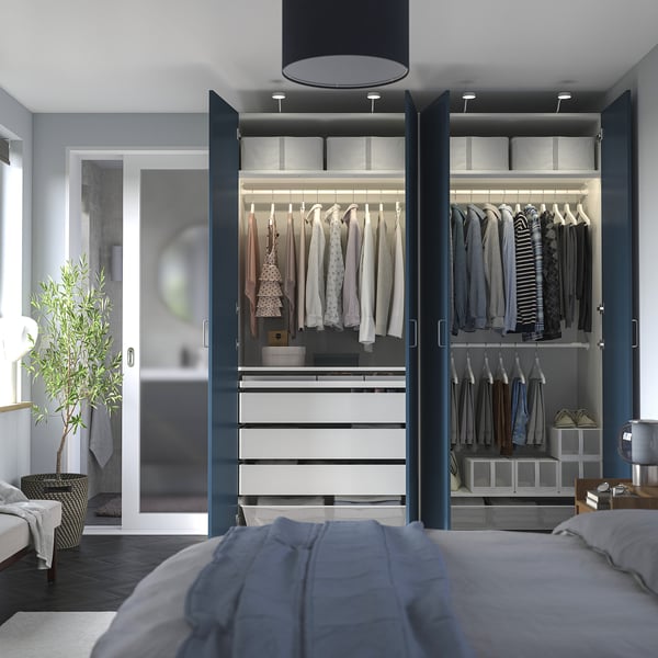Modern bedroom with open PAX wardrobe, organised clothes, and lighting.