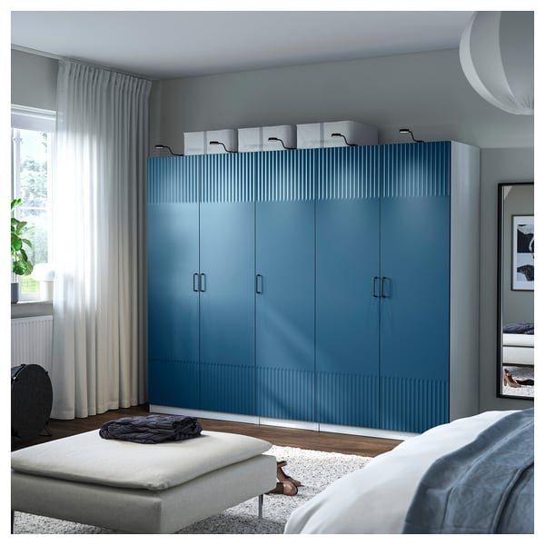 Modern bedroom with large blue PAX wardrobe, bed, and white curtains.