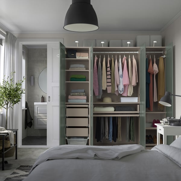 Modern bedroom featuring open PAX wardrobe displaying clothes, shelves, and drawers. Enclosed room with mirror and vanity visible through doorway.