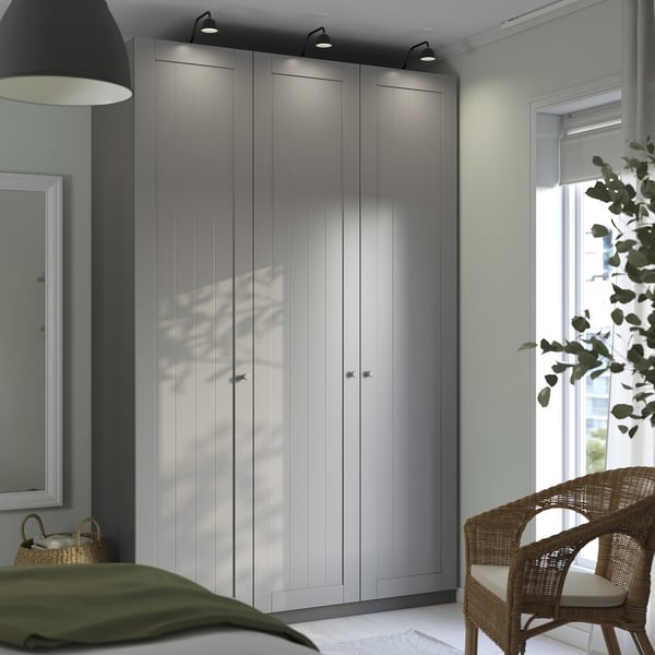 Modern bedroom with grey PAX wardrobe, wall lamp, window, wicker chair, and green bedspread.