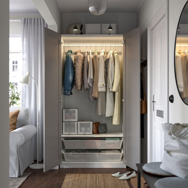 Open wardrobe with garments, lit shelves, and storage drawers, located in a small, cosy room with edge-lit mirror and seating.