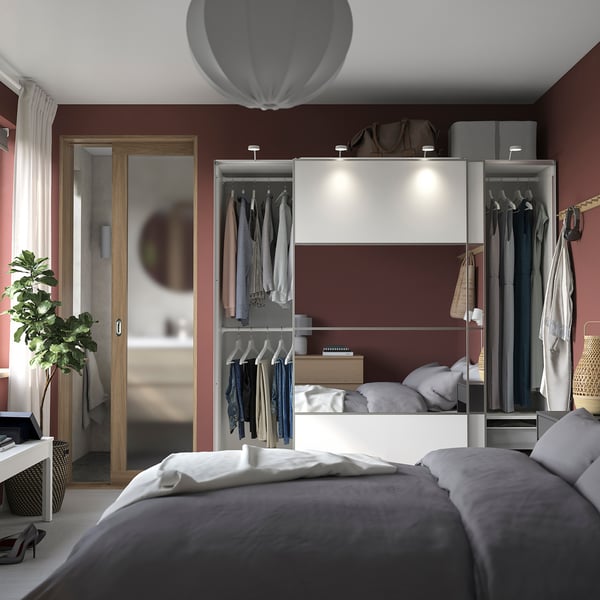 Modern bedroom with maroon walls, white linens, PAX wardrobe, mirror, pendant light.