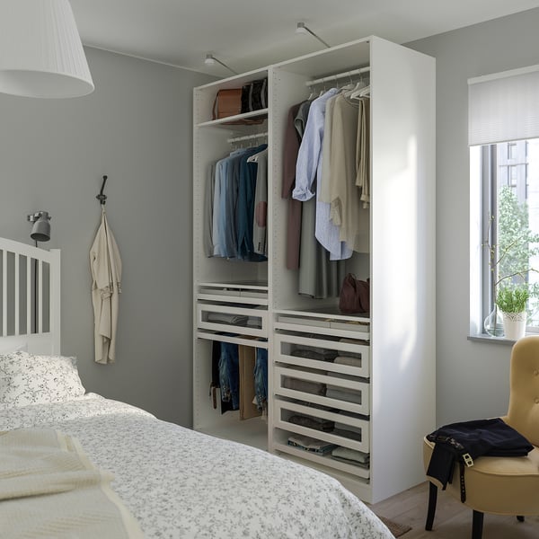 Modern bedroom with white PAX wardrobe against grey wall, filled with clothes. White-patterned bed nearby.