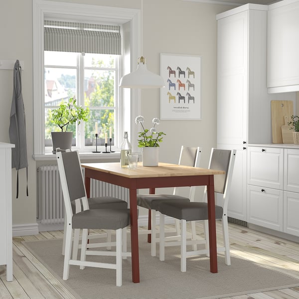 Small, modern dining set with wooden table and grey cushioned chairs, positioned neatly under a window, between white kitchen cabinets.