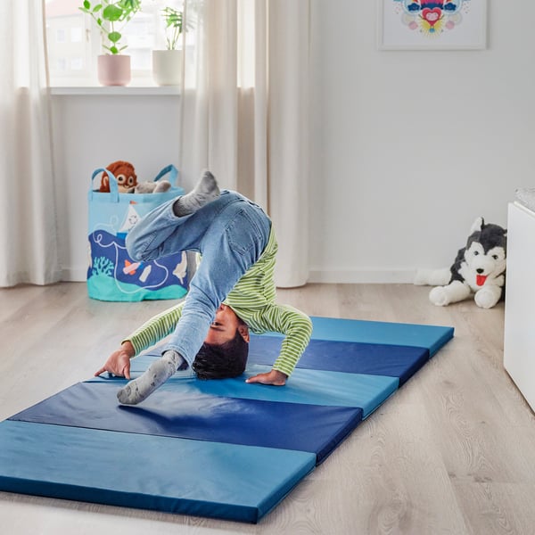Person doing yoga on blue mat in living room. Stuffed husky on floor nearby.