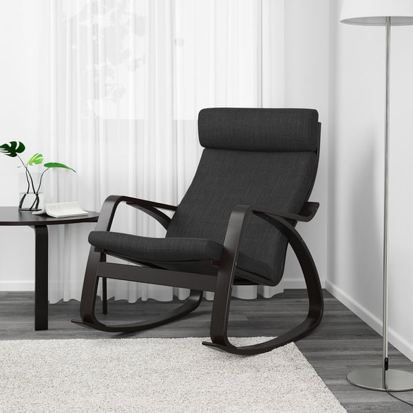 Modern black rocking chair with cushioned seat & back on light rug, beside table & lamp.