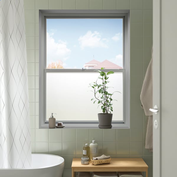 Modern bathroom with large window featuring neutral-toned PUCKELFLY window film, plant, and towel.