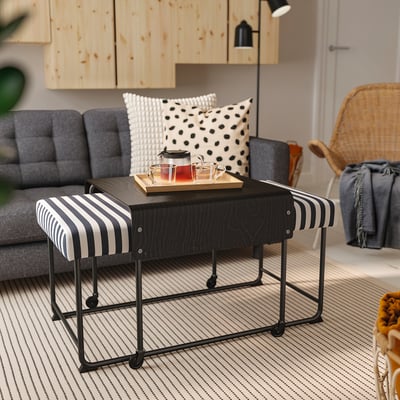 Modern living room with RÄVSAL black striped bench, grey cushioned sofa, wooden cabinets, and wicker chair on striped rug.