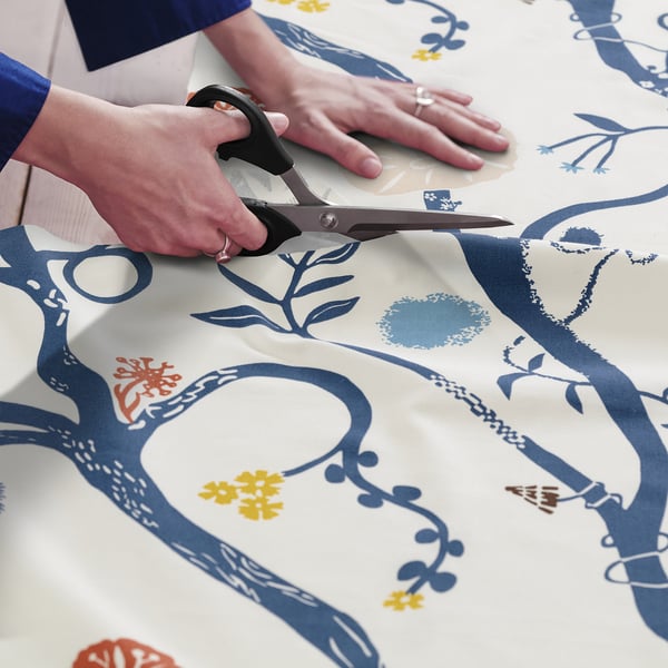 A person cuts colourful, patterned fabric with scissors, preparing for a sewing project.