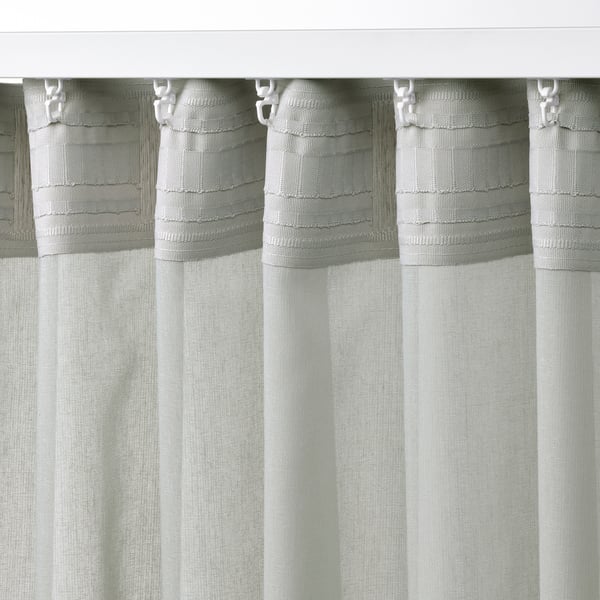 A close-up of sheer light grey curtains with white tabs hanging neatly, designed to philtre light and provide privacy.