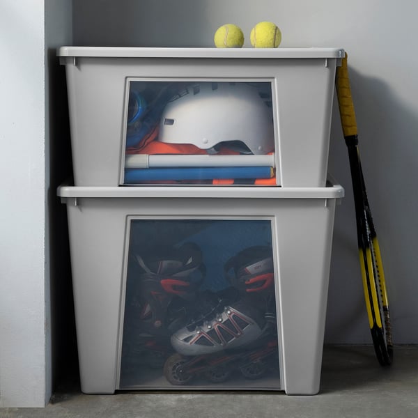 Grey SAMLA storage bins, one stacked, hold sports gear. Tennis rackets lean against it.