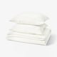 Stacked white bedding set, including folded duvet and pillows, featuring soft, textured muslin fabric.