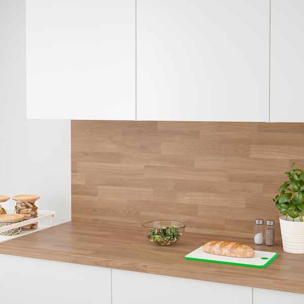 Modern kitchen counter with wooden backsplash. Bread, greens, containers, and plant sit on the counter.