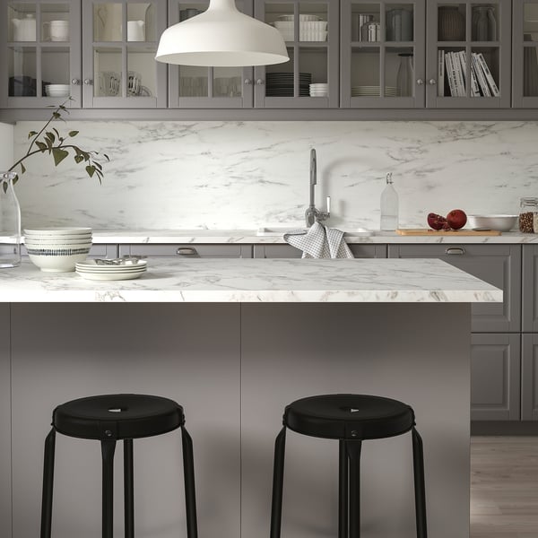 Modern kitchen with marble countertops, grey cabinets, black stools, and white pendant light. Custom-made wall panel protects walls.