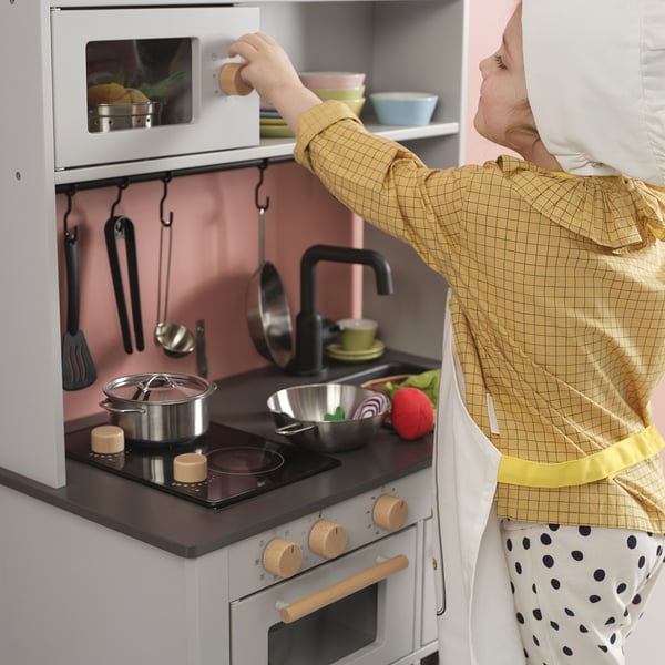 Child playing with toy kitchen, using microwave.