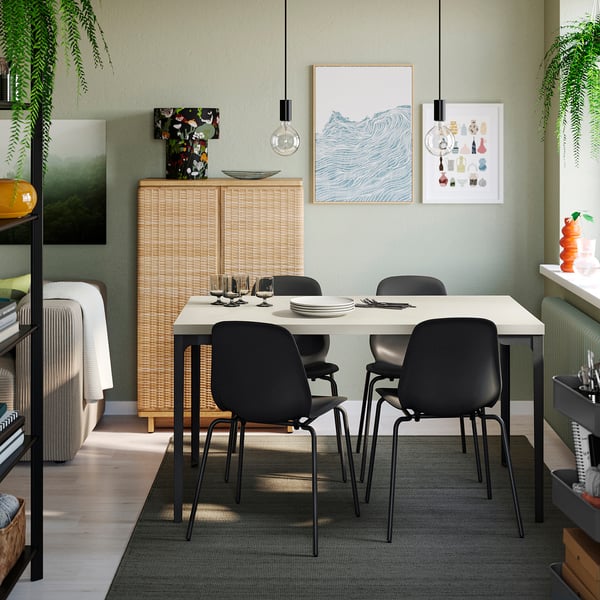 Modern dining area SKÅLSTA white table surrounded by black chairs. Wall-mounted rattan cabinet, greenery, and colourful artwork enhance the decor.