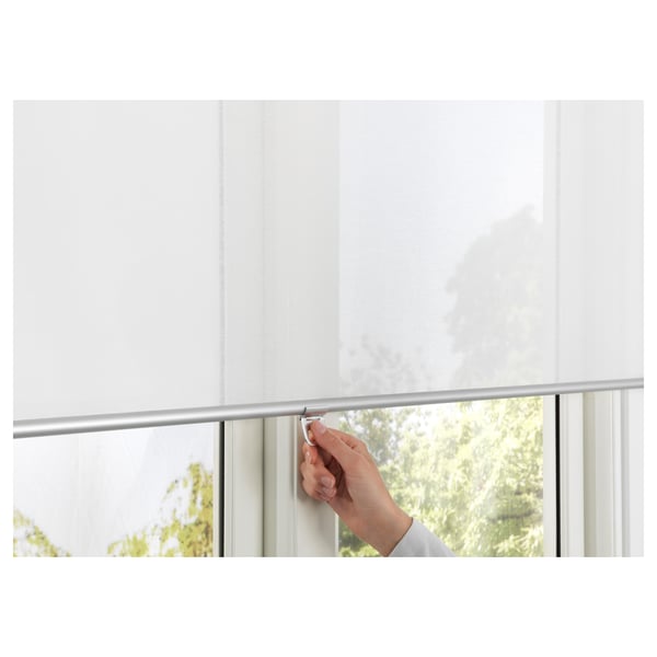 Hand lowers roller blind over window, safely and softly filtering light with SKOGSKLÖVER.