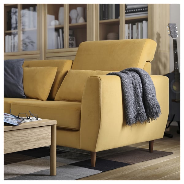 Modern yellow sofa with wooden legs, grey throw blanket, in cosy living room setup.