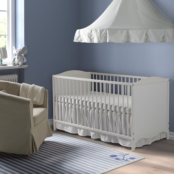 White nursery cot, small blue rug, beige chair, elephant toy, blue wall.