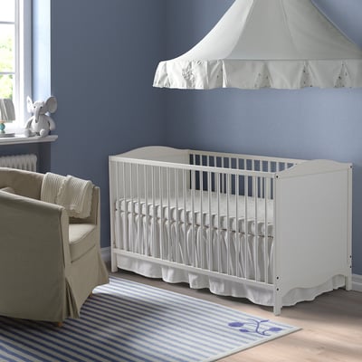 White nursery cot, small blue rug, beige chair, elephant toy, blue wall.