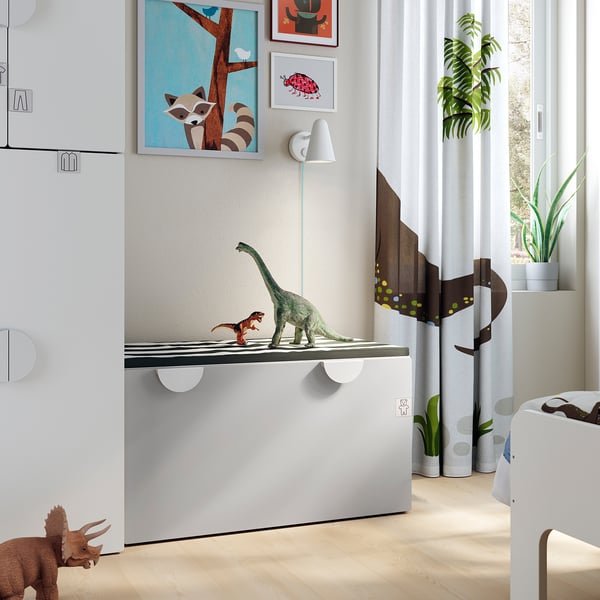 A childs room with dinosaur toys on a white SMÅSTAD bench, featuring modern decor and a large window.