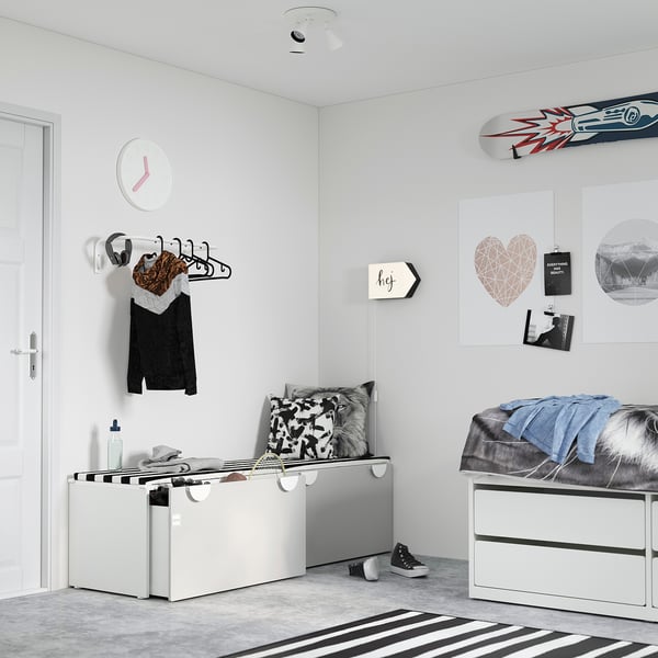 Modern bedroom with white SMÅSTAD storage and bench, striped rug, wall clock, decorative posters, headphones, and clothing on hangers.