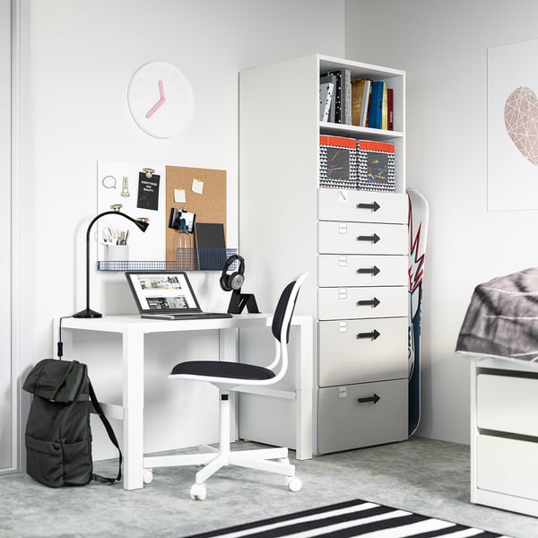 A modern students bedroom with a white SMÅSTAD desk, black chair, and grey storage unit featuring drawers and shelves.