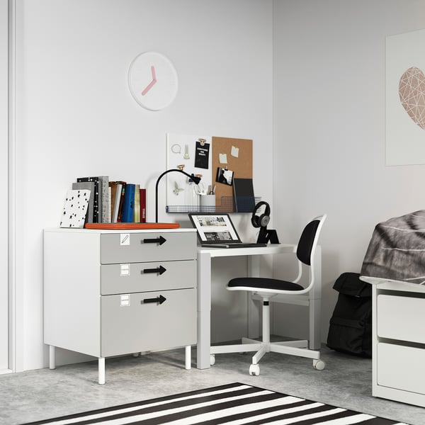 Small white desk, SMÅSTAD, with grey drawers in bedroom corner. Laptop, books, and chair placed on it. Modern, minimalist design.