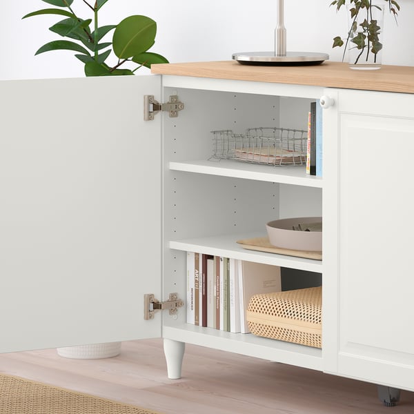 White cabinet with open door, baskets, bowls, books, plant top.