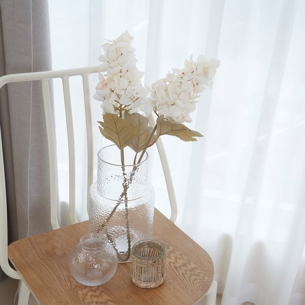 A wooden side table holds a clear vase with light-colored flowers; next to it are two small glass containers.