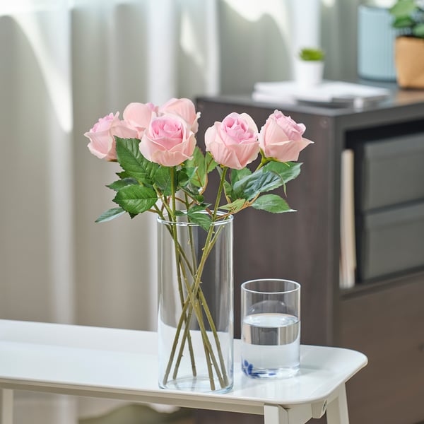 Small clear vase with pink roses on a tiny table.