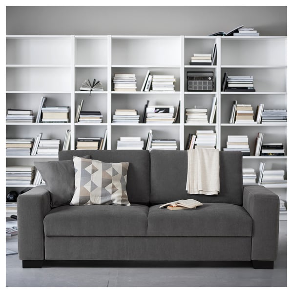 Modern dark grey sofa with geometric cushions against a white bookshelf filled with books.