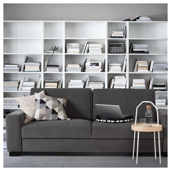 Modern living room with grey SÖRVALLEN sofa, cushions, laptop, and wooden side table against bookshelf.