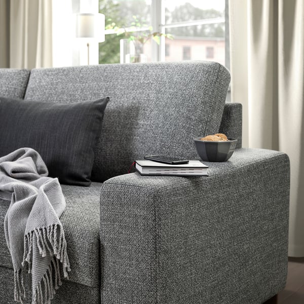 A cozy gray sofa with a dark pillow, draped blanket, and a bowl with a book and remote on the armrest.