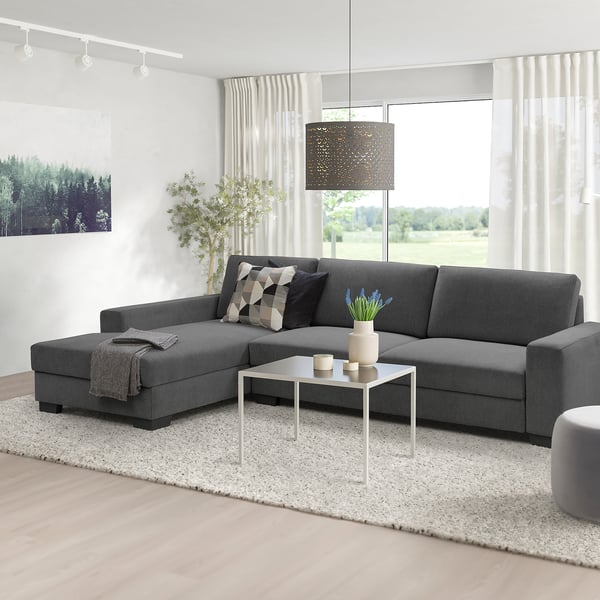 Modern grey l-shaped SÖRVALLEN sofa, minimalist design. Centred under a hanging lamp, larger than side table & plant, cosy & spacious.