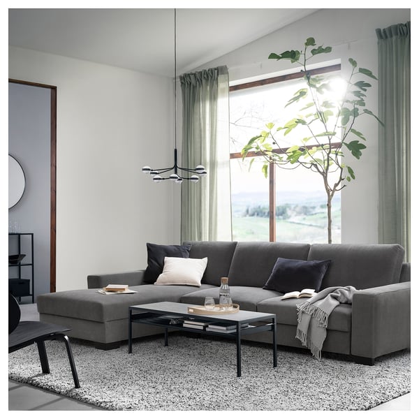 Modern living room with a dark grey SÖRVALLEN sectional sofa, black coffee table, large windows, and a tall green plant.