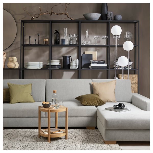 Modern minimalist living room with grey SÖRVALLEN sofa, wooden side table, and black metal shelves decorated with various home decor items.