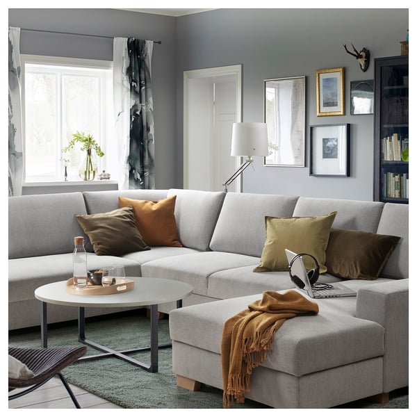 Modern grey l-shaped sofa with colourful pillows, coffee table, and cosy decor in stylish living room with large windows.