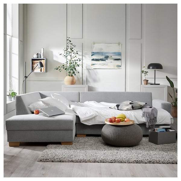 Modern living room featuring a grey SÖRVALLEN sofa with white pillows, grey ottoman, and minimalist decor.
